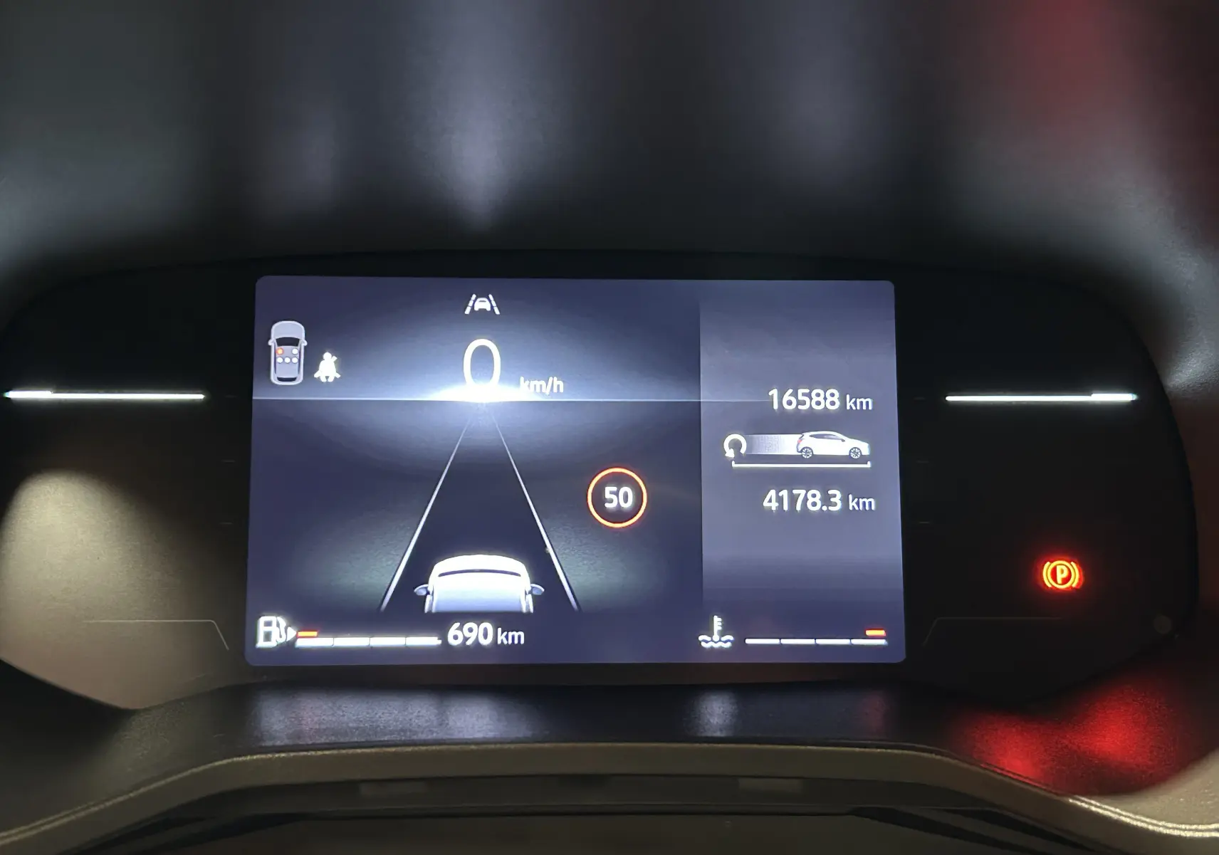 Vue rapprochée du tableau de bord numérique de la Renault Clio V blanc, affichant la vitesse à 0 km/h et l'autonomie restante.