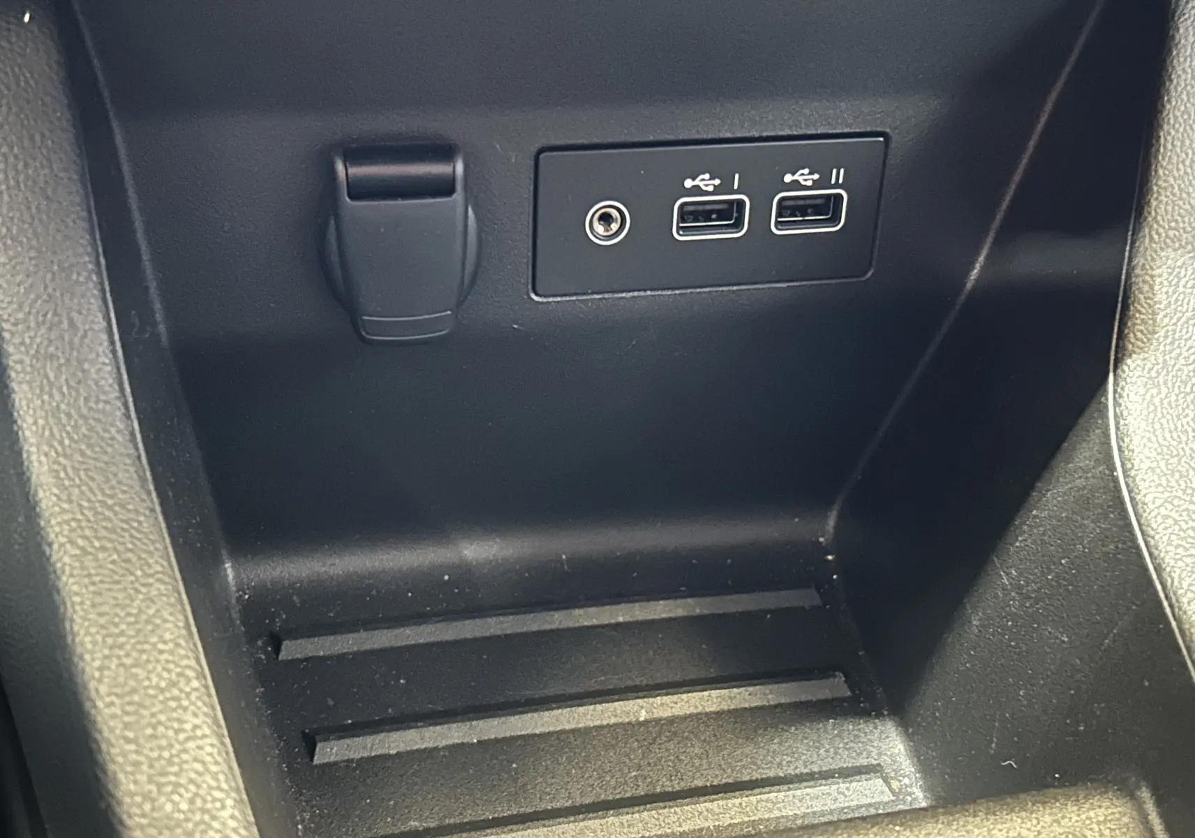 Vue rapprochée de la console centrale noire avec prises USB et prise jack dans une Renault Clio V blanche.