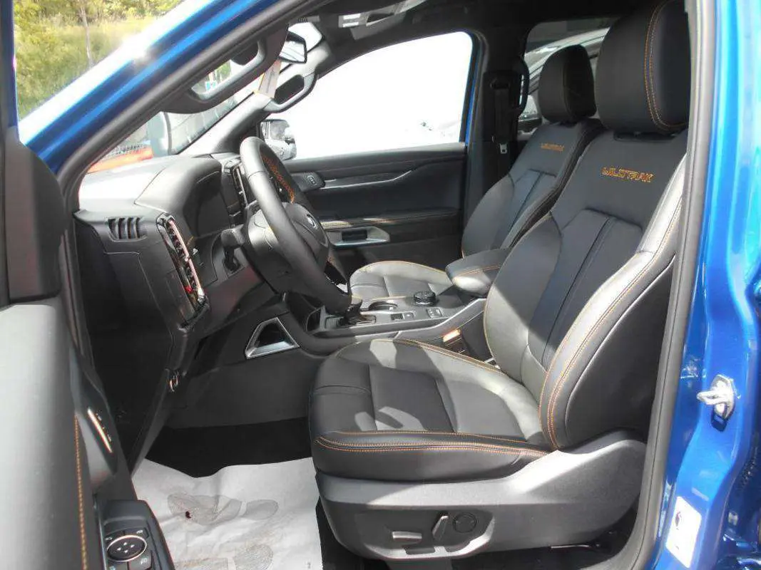 Intérieur du Ford Ranger 2025 bleu lightning vu côté gauche, sièges cuir noirs avec surpiqûres orange et logo Wildtrak.