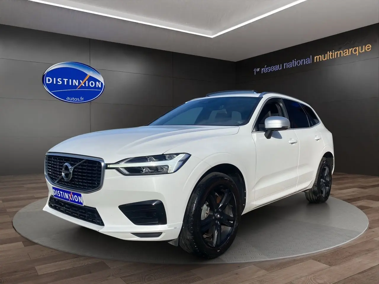 Volvo XC60 D4 R-Design blanc en 3/4 avant droit avec jantes noires et calandre distinctive noire.