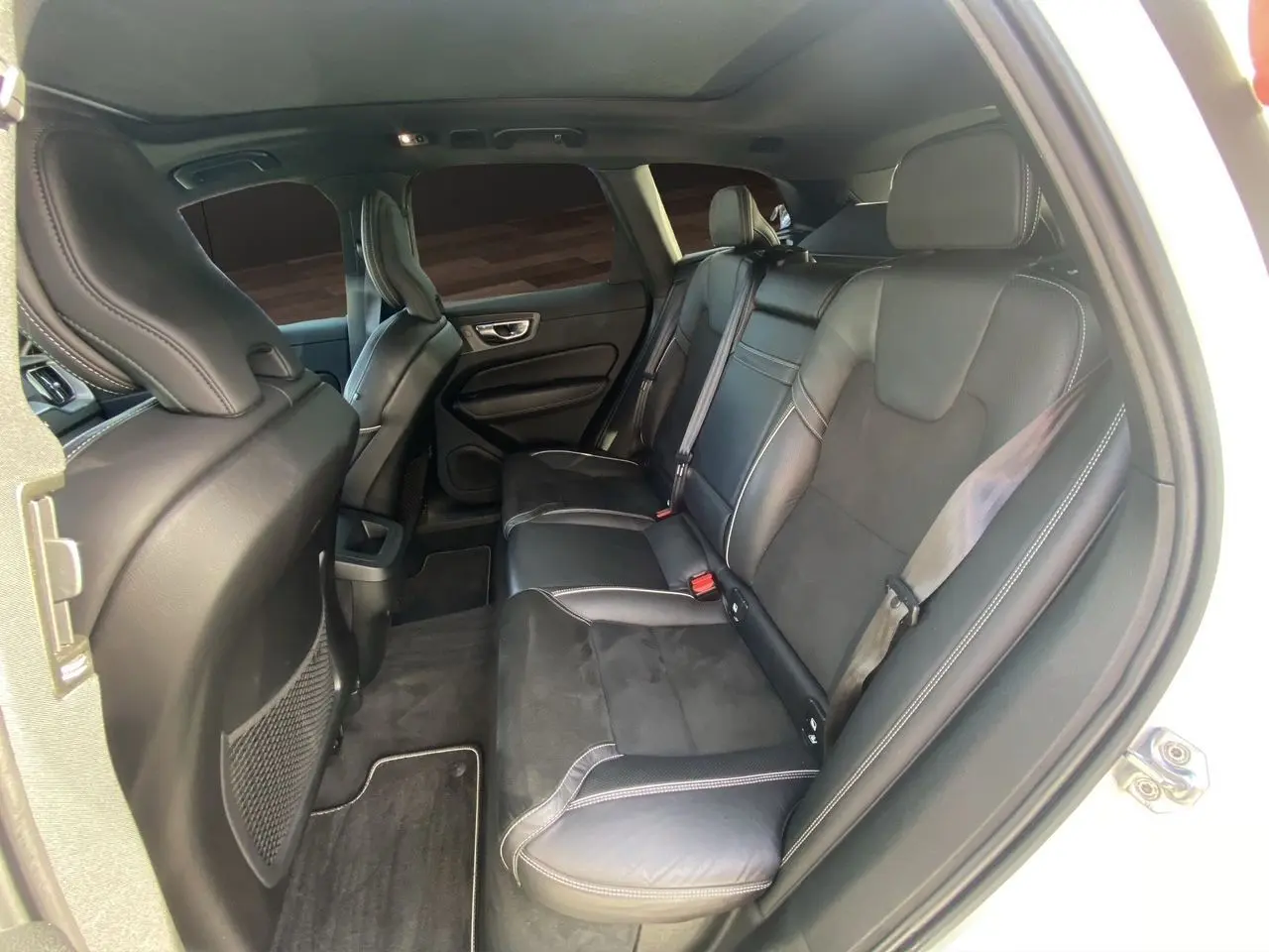 Vue intérieure arrière droite du Volvo XC60 blanc 2019, sièges en cuir noir avec surpiqûres contrastées.