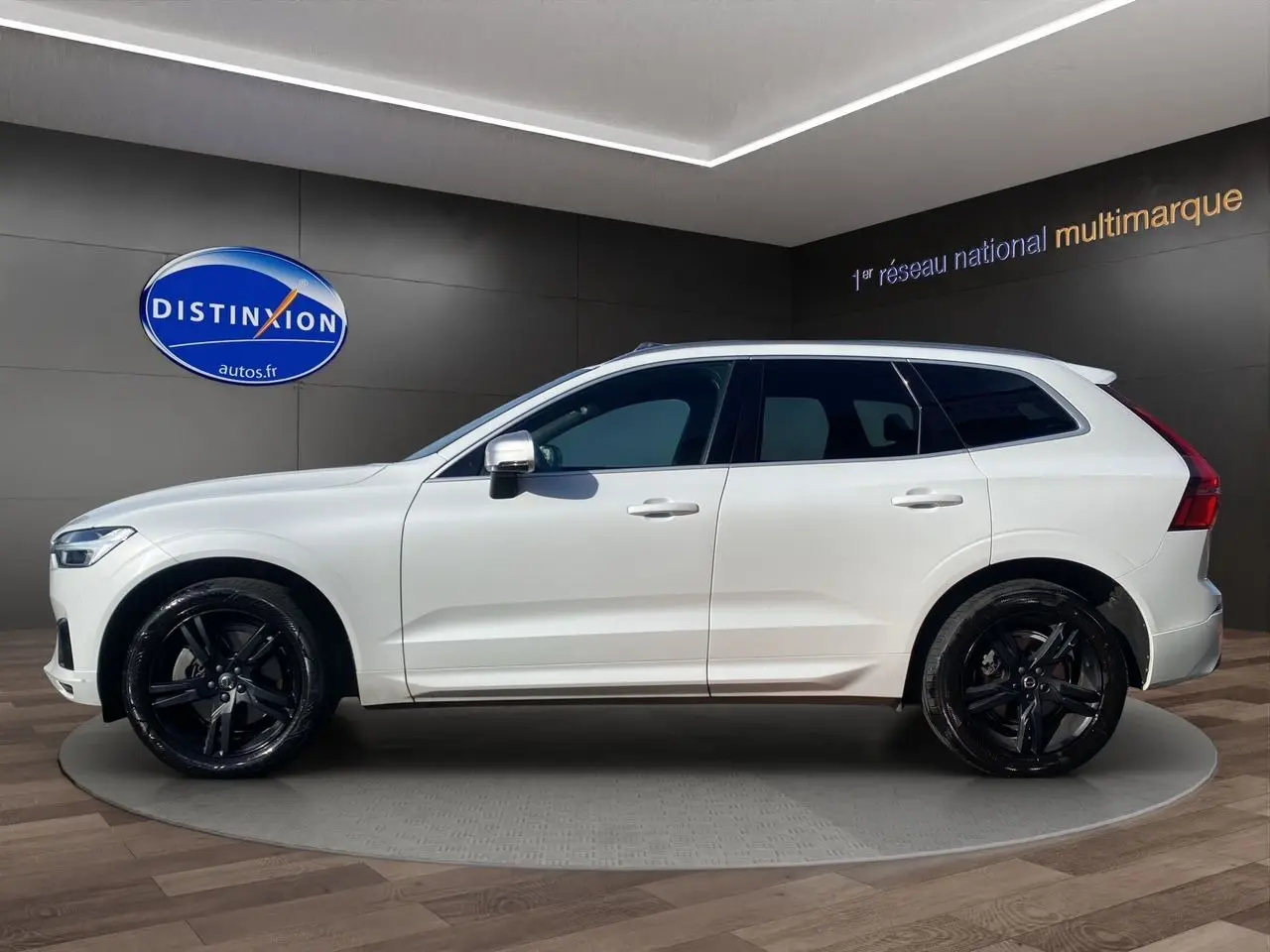 Profil droit d'un Volvo XC60 blanc 2019 avec jantes noires et rétroviseurs chromés en showroom.