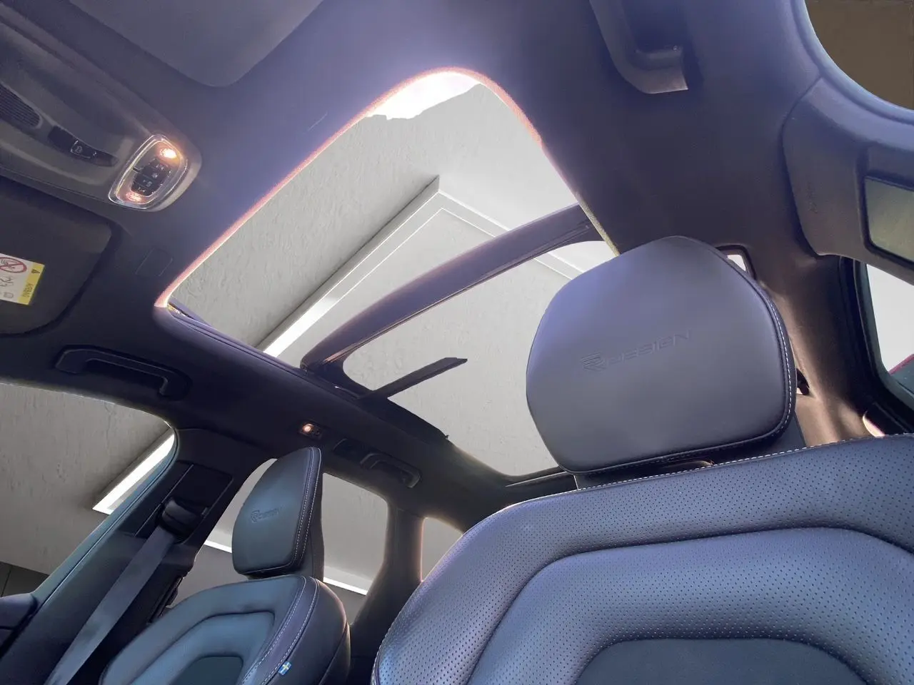 Vue intérieure du toit ouvrant panoramique et sièges avant en cuir noir embossé R-DESIGN du Volvo XC60 blanc 2019.