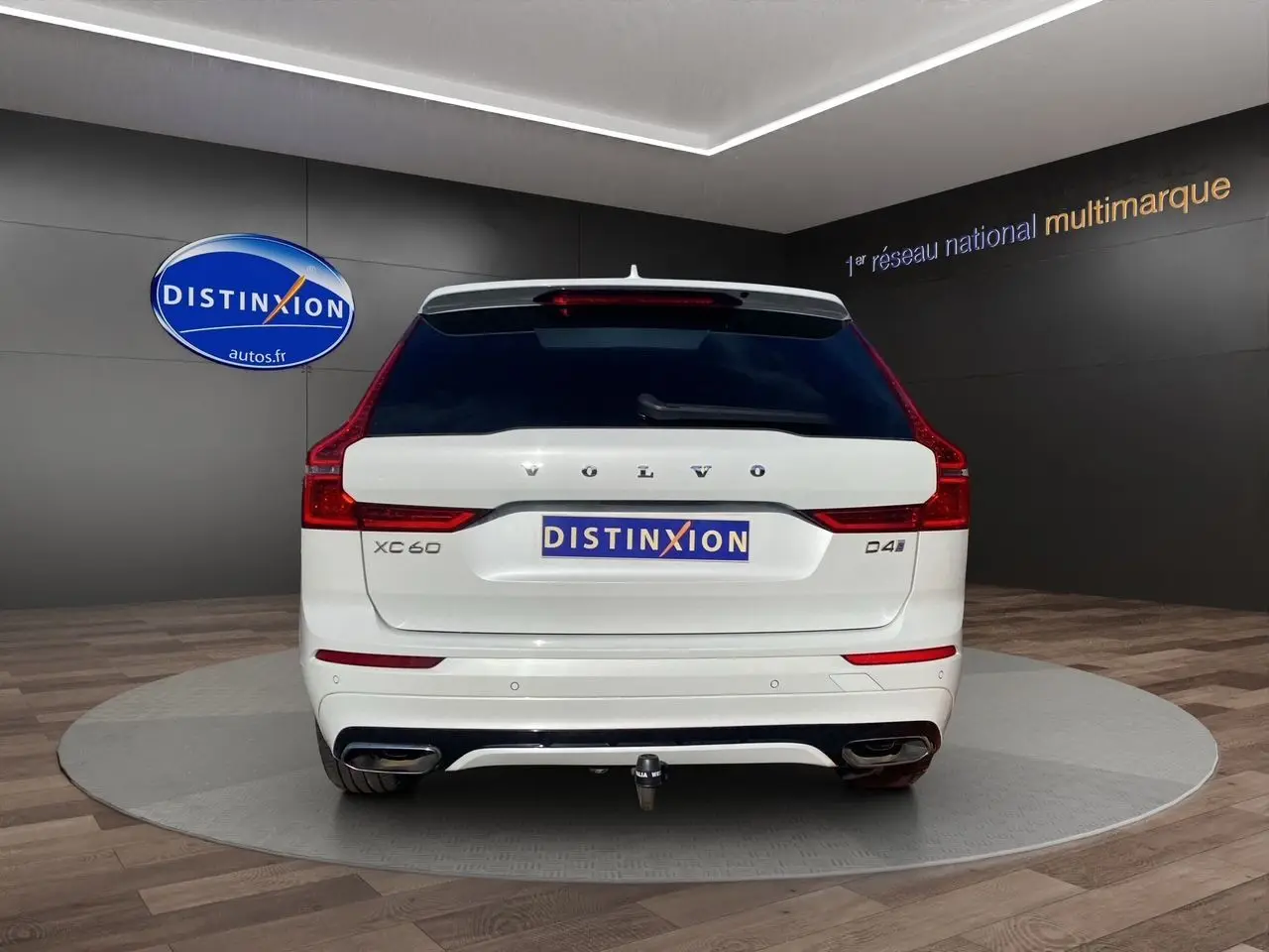 Vue arrière d'un Volvo XC60 D4 blanc avec attelage et feux arrière LED dans un showroom.