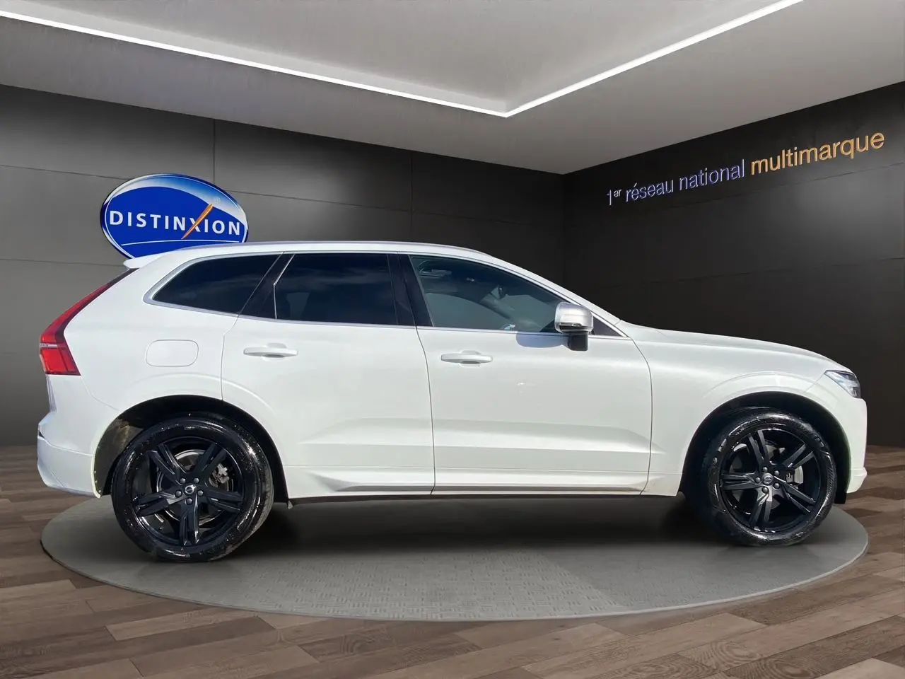 Vue latérale droite du Volvo XC60 blanc 2019 R-Design avec jantes noires et vitres teintées en showroom.