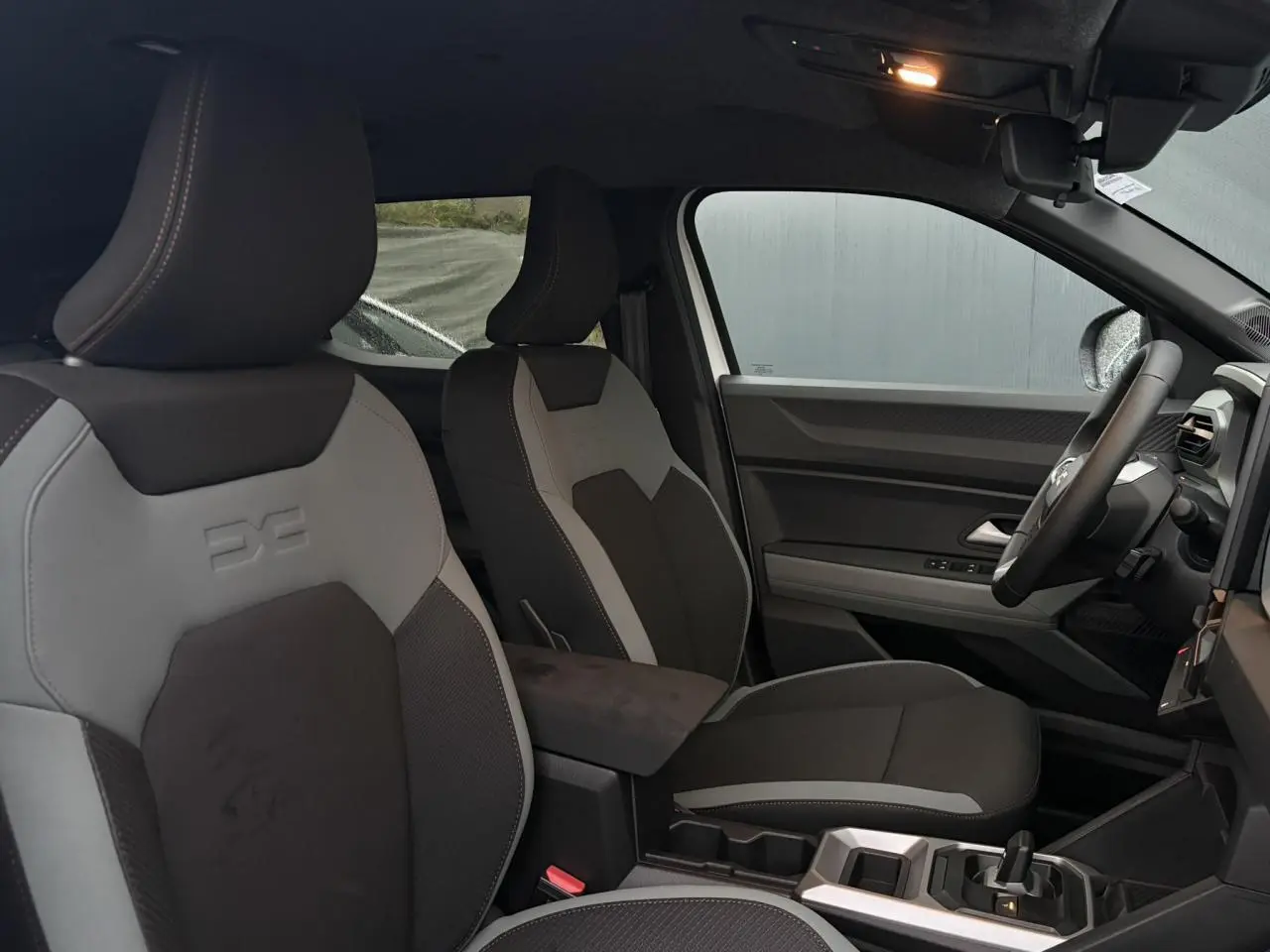Vue intérieure côté droit du Dacia Duster 2026 Hybrid blanc Glacier, montrant les sièges bicolores et la console centrale moderne.