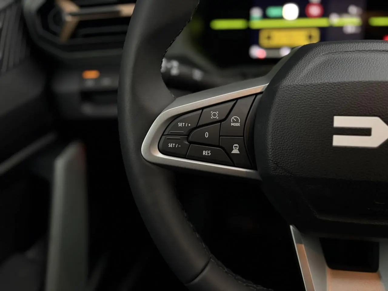 Gros plan sur les commandes au volant noir du Dacia Duster 2026, avec finition argentée et logo partiel visible.