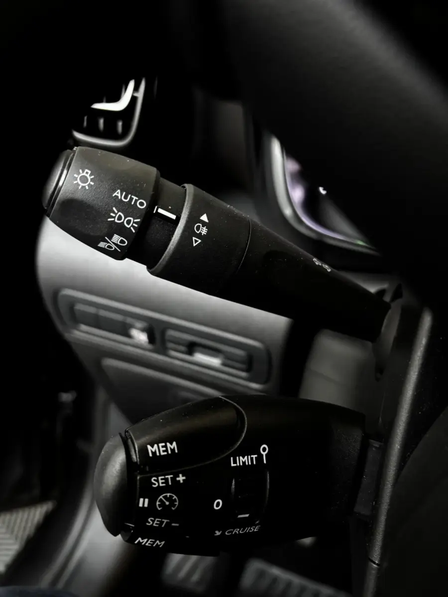 Gros plan sur les commandes au volant du Citroën C3 Aircross gris clair, mettant en valeur les réglages des phares et du régulateur de vitesse.