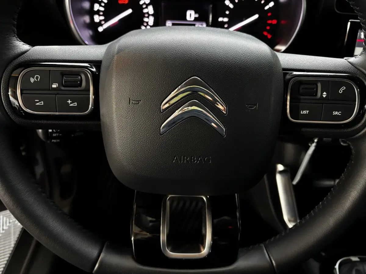 Gros plan sur le volant cuir noir du Citroën C3 Aircross 2024 avec commandes intégrées et logo chromé central.