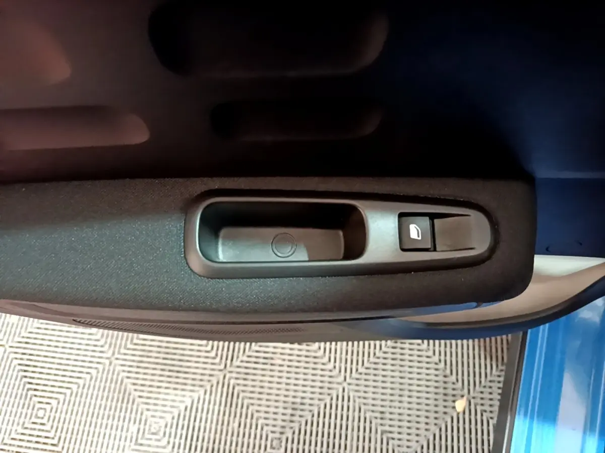 Gros plan sur la commande de lève-vitre côté conducteur d'une Citroën C3 bleue, intérieur tissu noir.
