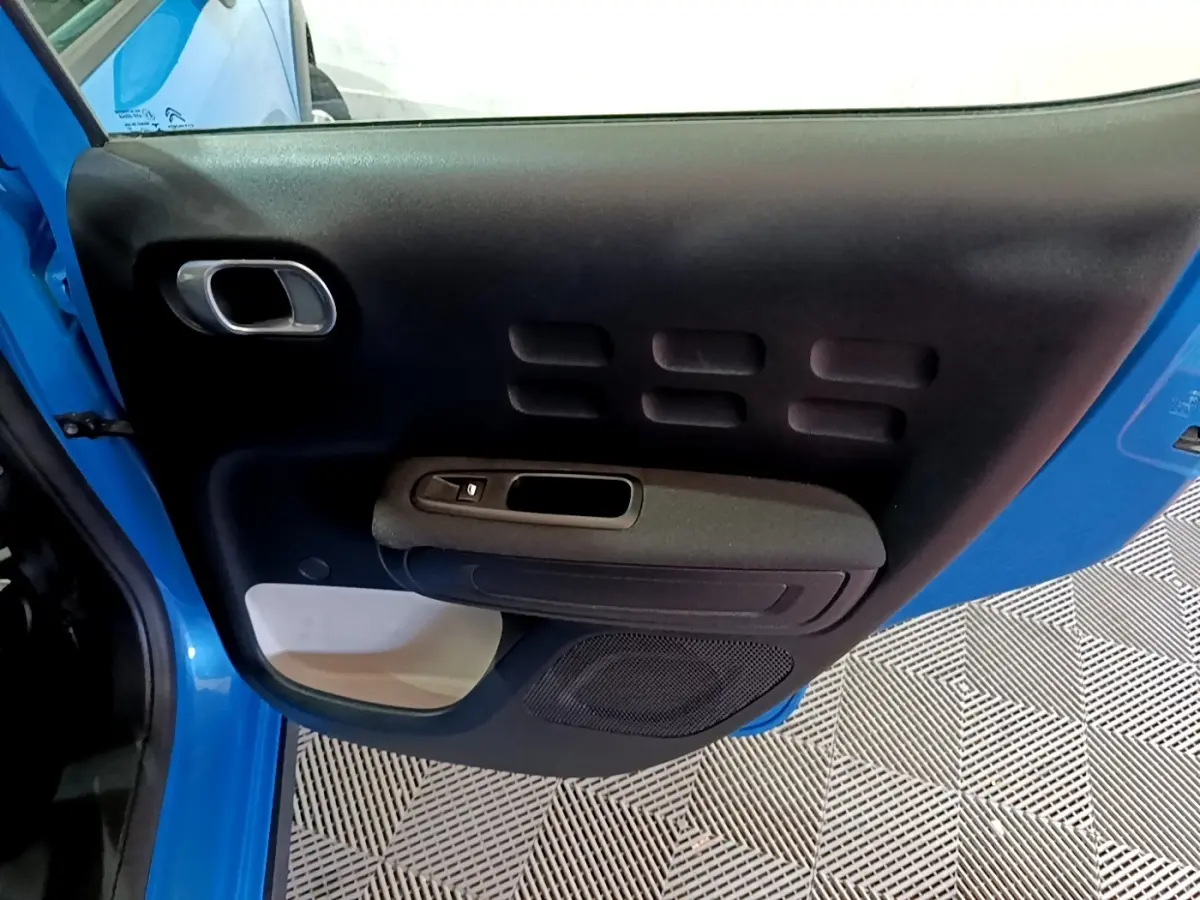 Vue intérieure de la porte avant gauche bleu de la Citroën C3 2017 avec poignée et commande de vitre électrique.