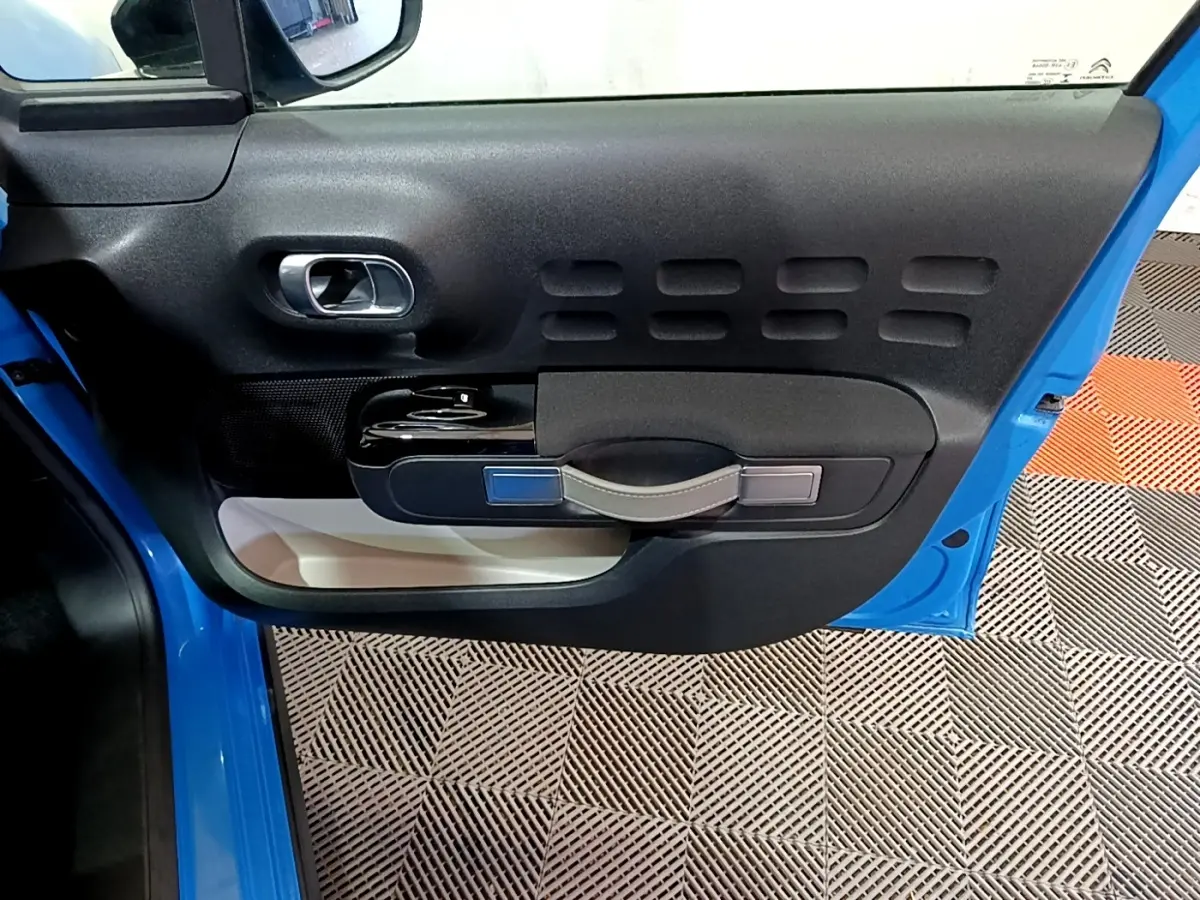 Vue intérieure de la porte avant gauche bleu vif de la Citroën C3 avec poignée et commandes de vitre noires.