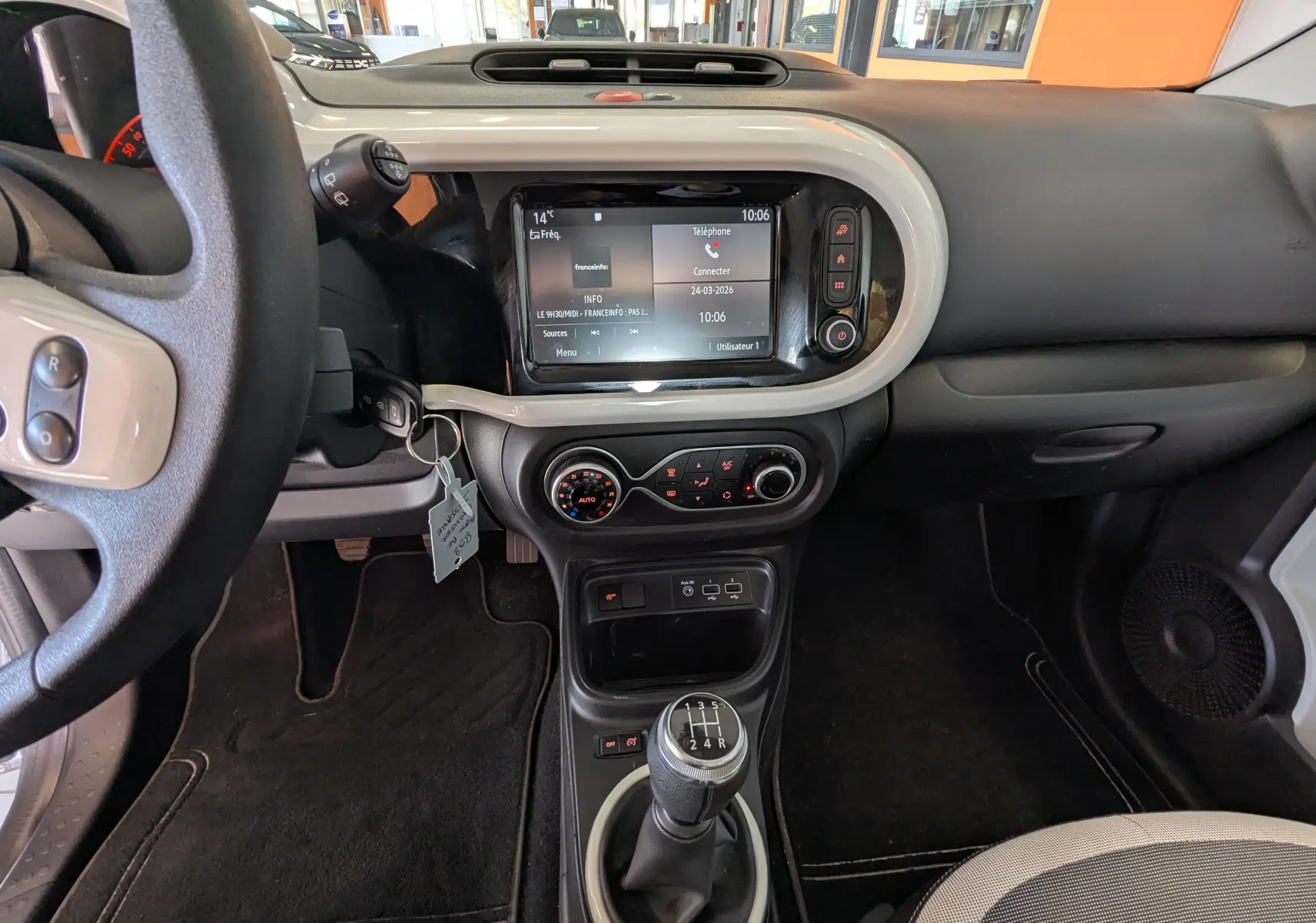 Vue intérieure du tableau de bord de la Renault Twingo III gris cassiopée, avec écran tactile et levier de vitesse manuel visible.