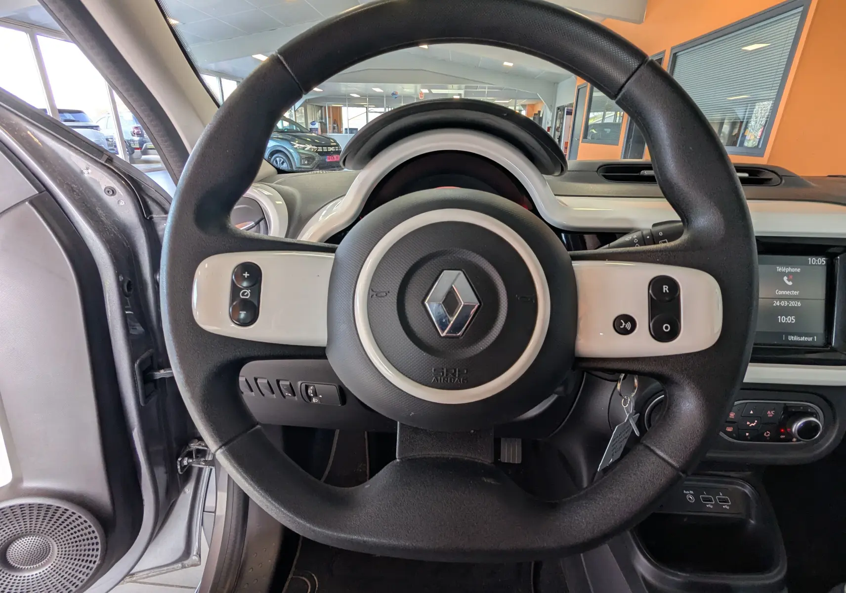 Vue intérieure centrée sur le volant noir et blanc de la Renault Twingo III gris Cassiopée, avec tableau de bord et écran tactile visibles.