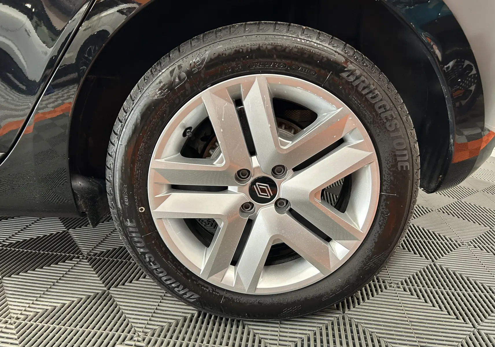 Gros plan sur la roue arrière droite d’une Renault Clio V noire, avec une partie de la carrosserie brillante visible.