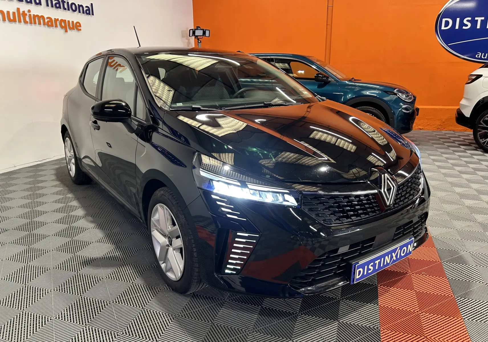 Renault Clio V noire vue en 3/4 avant droit, phares LED allumés, calandre distinctive et intérieur visible.