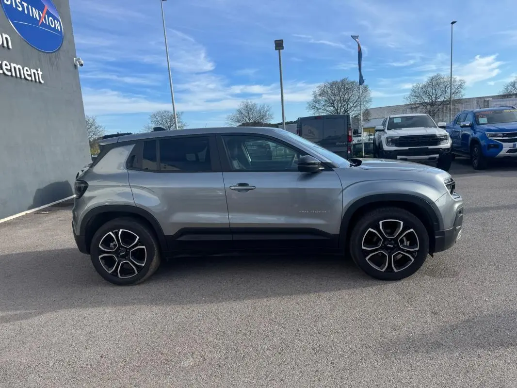 Vue de profil côté gauche d'un Jeep Avenger gris 2025 avec jantes distinctives et lignes noires sur les bas de caisse.