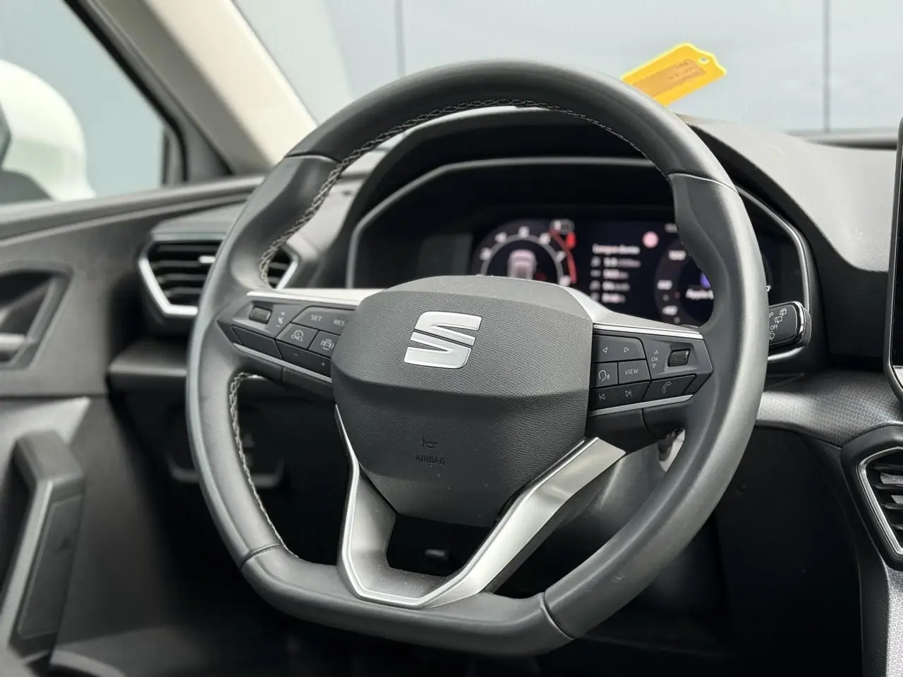 Vue rapprochée du volant cuir multifonction noir avec logo SEAT, tableau de bord numérique en arrière-plan.