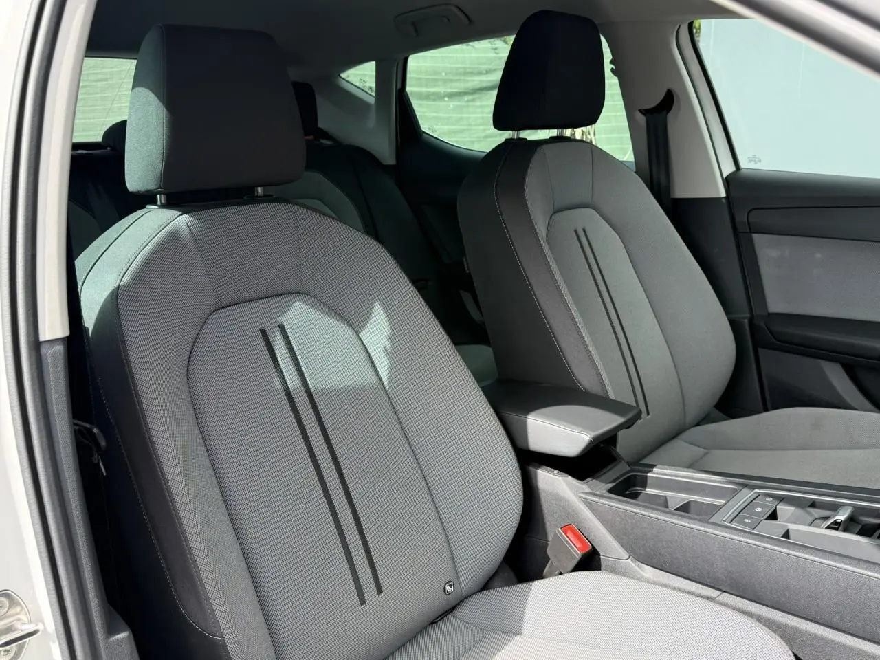 Vue intérieure côté conducteur du siège avant gris clair du SEAT LEON 2025 avec accoudoir central et console moderne.