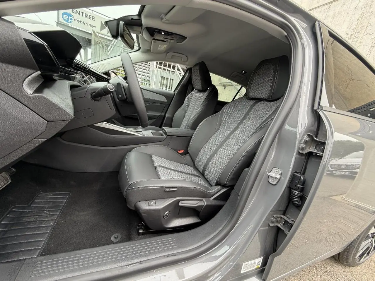 Vue intérieure côté conducteur de la Peugeot 308 gris sellenium, mettant en valeur les sièges en tissu et cuir avec surpiqûres.