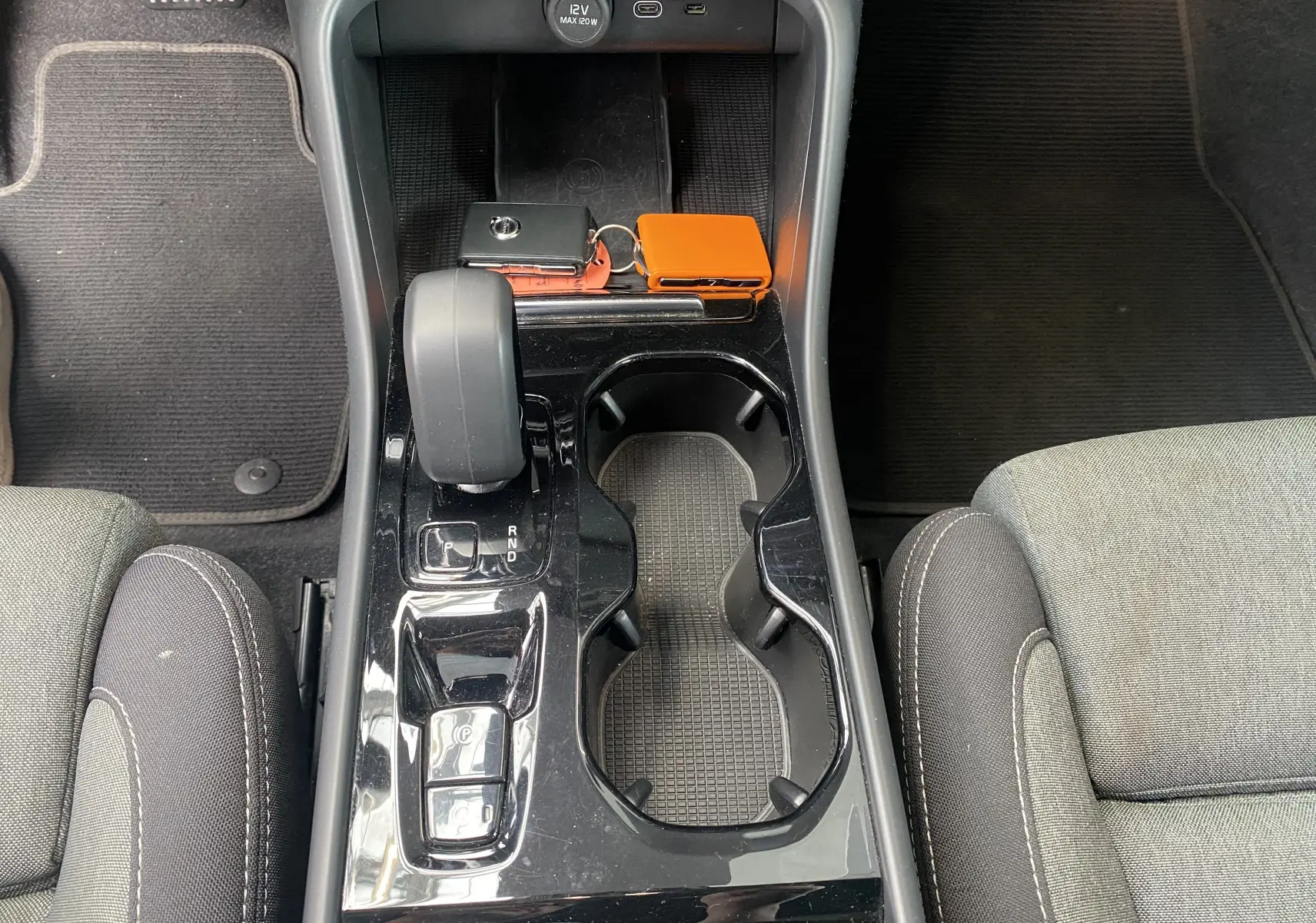 Vue plongeante sur la console centrale noire brillante du Volvo XC40 2023 avec levier de vitesse et porte-gobelets.