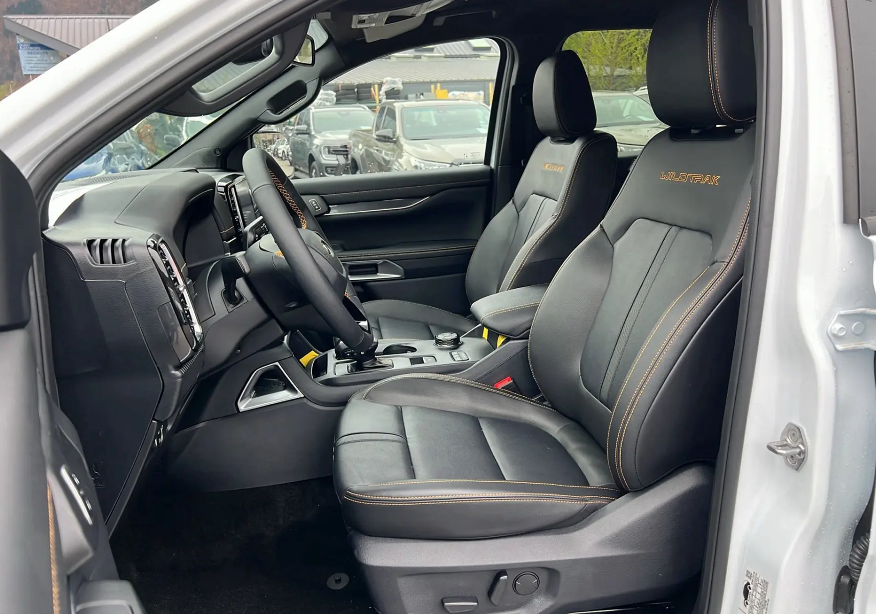 Intérieur du Ford Ranger 2025 blanc glacier, vue côté conducteur sur sièges cuir noirs avec surpiqûres orange Wildtrak.