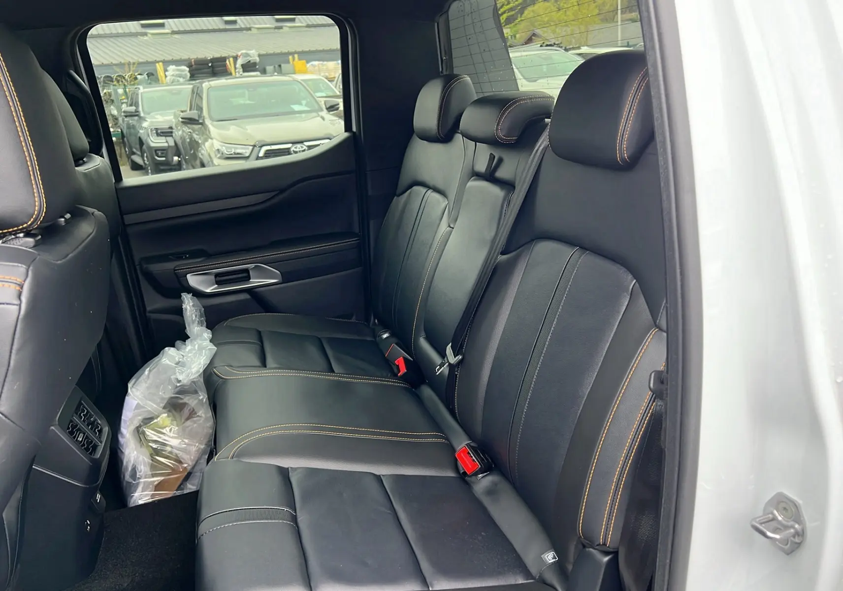 Vue intérieure côté droit sur la banquette arrière en cuir noir avec surpiqûres orange du Ford Ranger blanc glacier 2025 Wildtrak Plus.