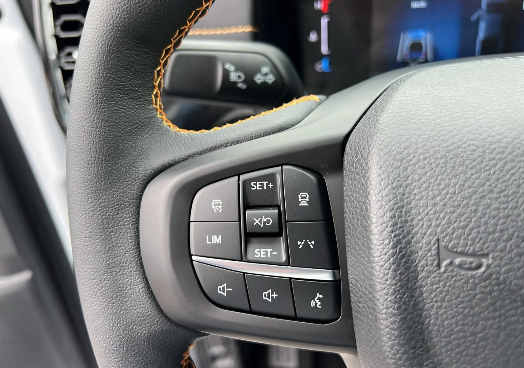 Gros plan sur le volant du Ford Ranger 2025 blanc glacier, montrant les commandes de régulateur et volume avec surpiqûres orange.