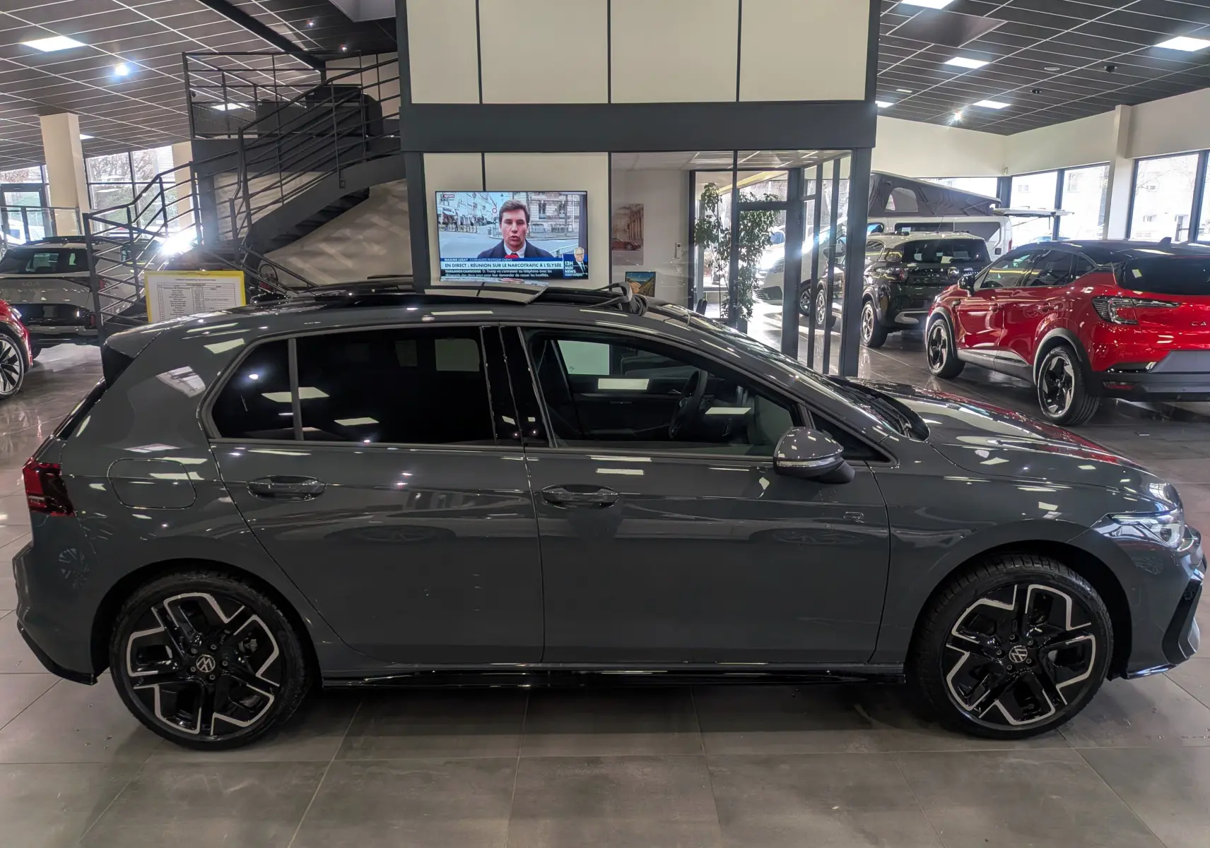 Vue de profil côté gauche d'une Volkswagen Golf gris dauphin R-Line avec jantes noires et toit ouvrant en concession.