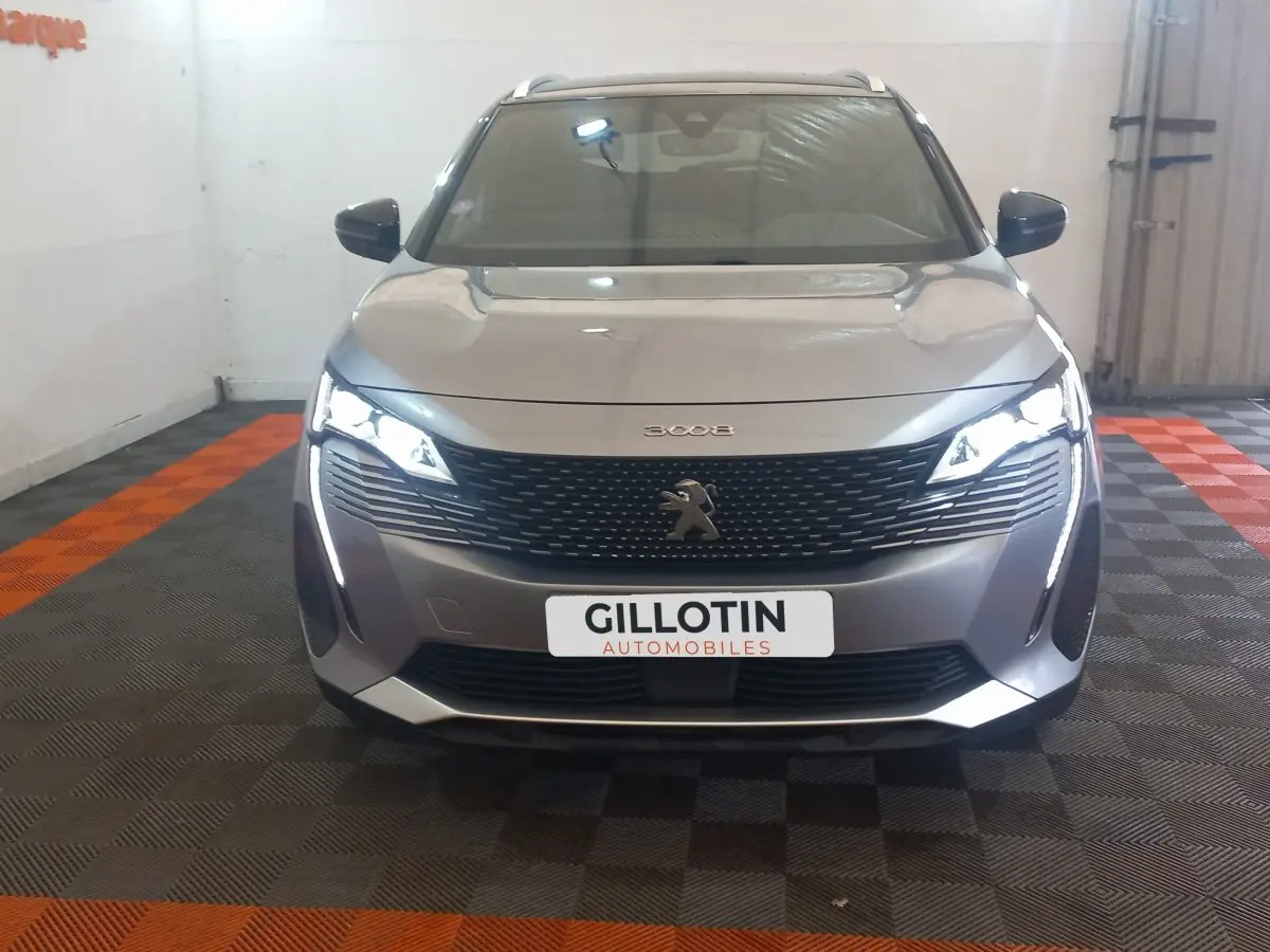 Vue frontale d'un Peugeot 3008 gris clair 2022 avec calandre noire et feux LED allumés en intérieur.