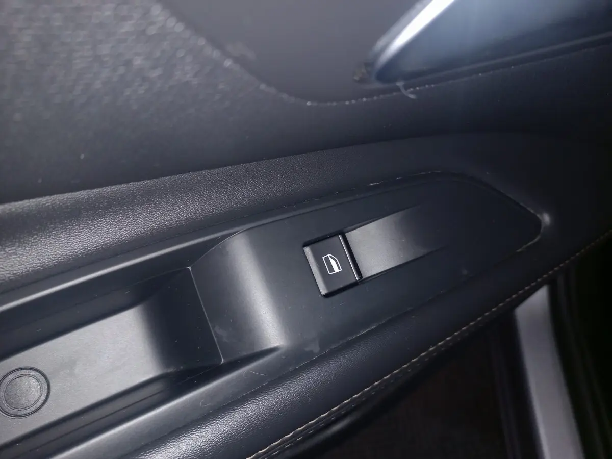 Gros plan sur le bouton de commande de la vitre électrique côté gauche, intérieur noir du Peugeot 3008 gris clair.
