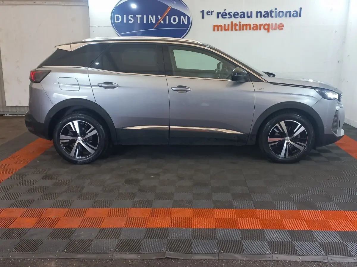 Vue de profil côté gauche d'un Peugeot 3008 GT gris clair 2022 avec jantes alliage et toit noir contrasté.