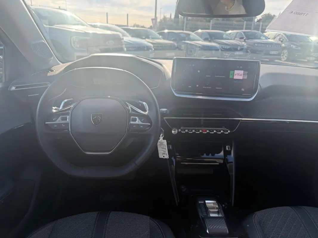 Vue intérieure frontale du poste de conduite de la Peugeot 208 Hybrid 110 e-DCS6 Allure 2024 avec écran tactile et volant compact noir.