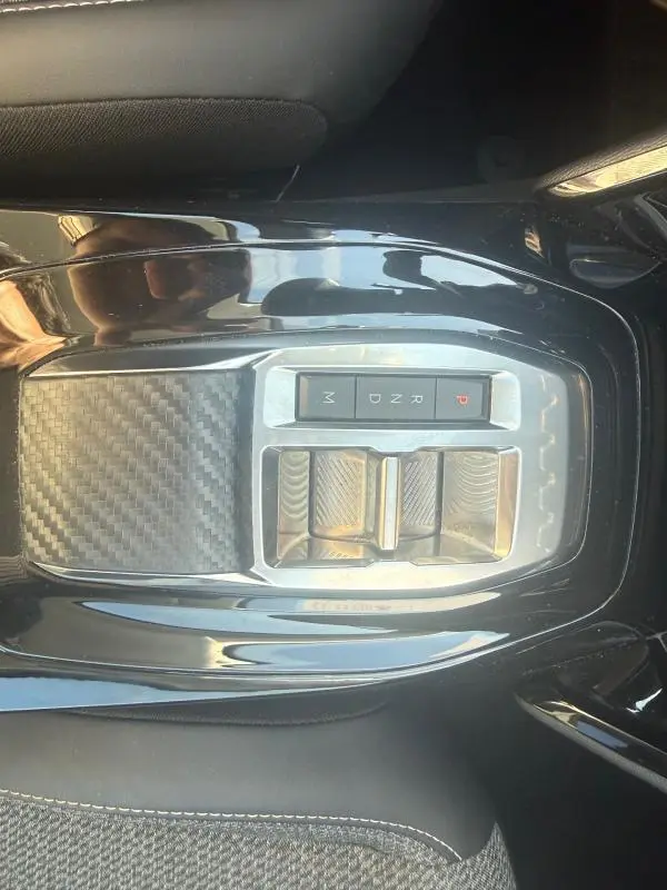 Vue plongeante sur la console centrale noire brillante de la Peugeot 208 Hybrid 110 e-DCS6 Allure 2024 avec commandes de boîte automatique.