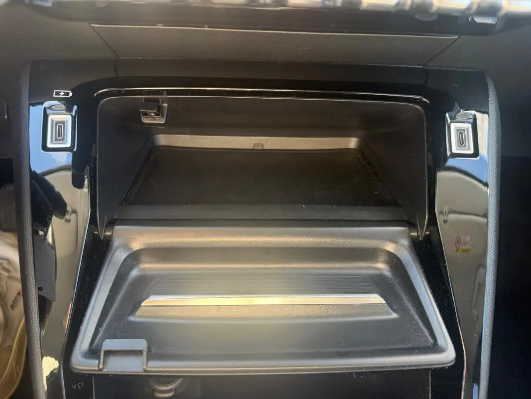 Vue rapprochée de la console centrale noire du Peugeot 208 Hybrid 110 e-DCS6 Allure 2024, avec compartiment ouvert.