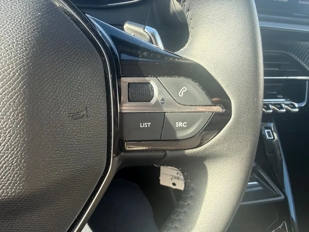 Gros plan sur les commandes gauche du volant noir de la Peugeot 208 Hybrid 110 e-DCS6 Allure 2024, intérieur moderne.