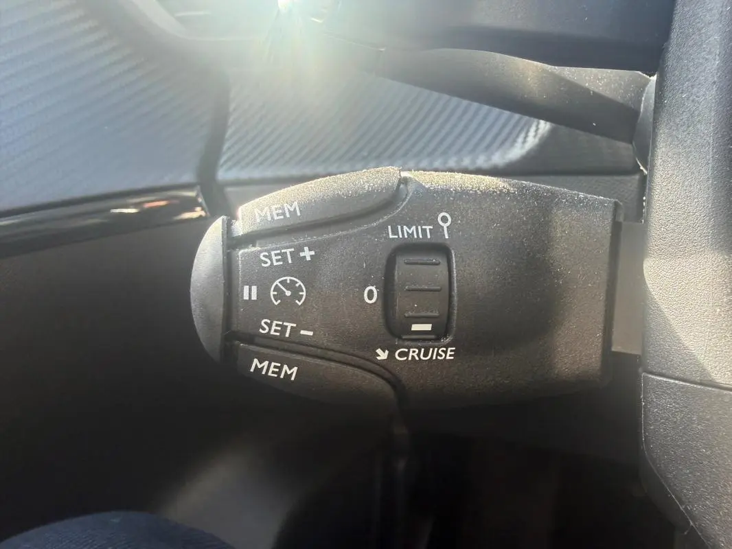 Gros plan sur la commande de régulateur de vitesse du Peugeot 208 blanc Hybrid 110 e-DCS6 Allure 2024.