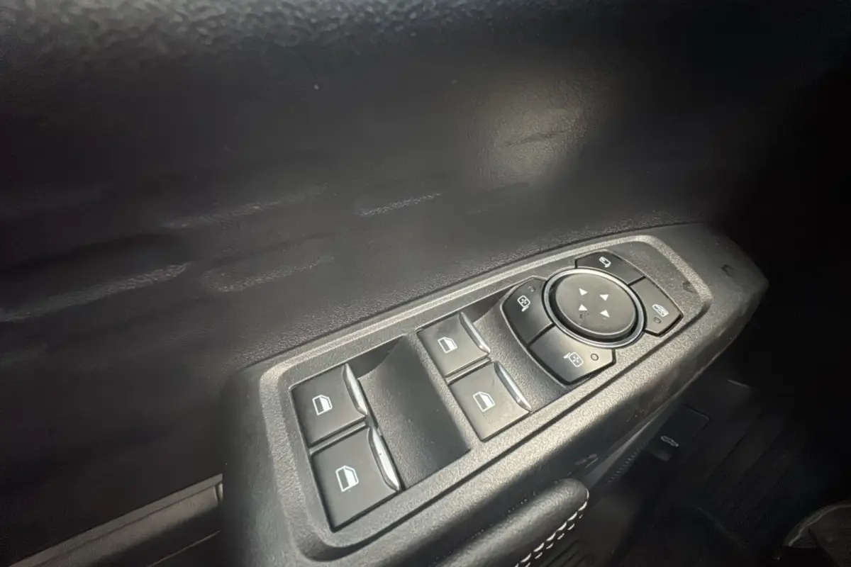 Gros plan sur les commandes des vitres électriques et rétroviseurs côté conducteur du Ford Ranger gris commandeur.