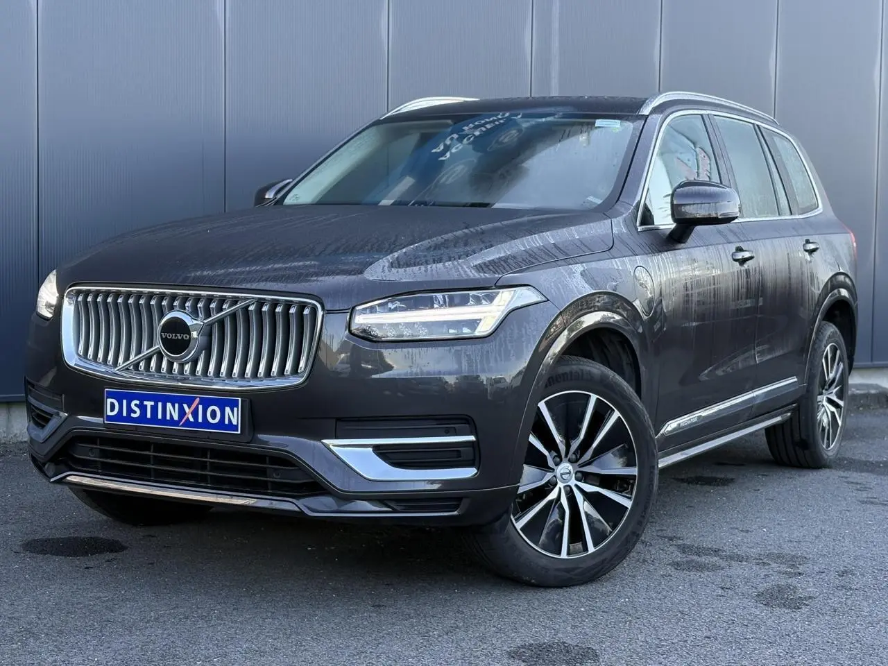 Volvo XC90 T8 hybride gris Platinium en 3/4 avant droit avec jantes alliage et calandre chromée distinctive.