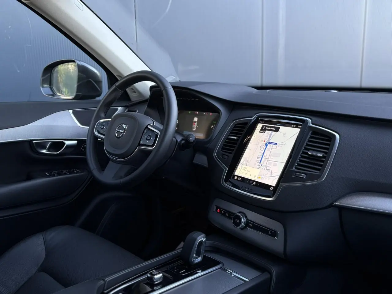 Vue intérieure côté conducteur du Volvo XC90 2024 avec écran tactile vertical et volant multifonction noir.
