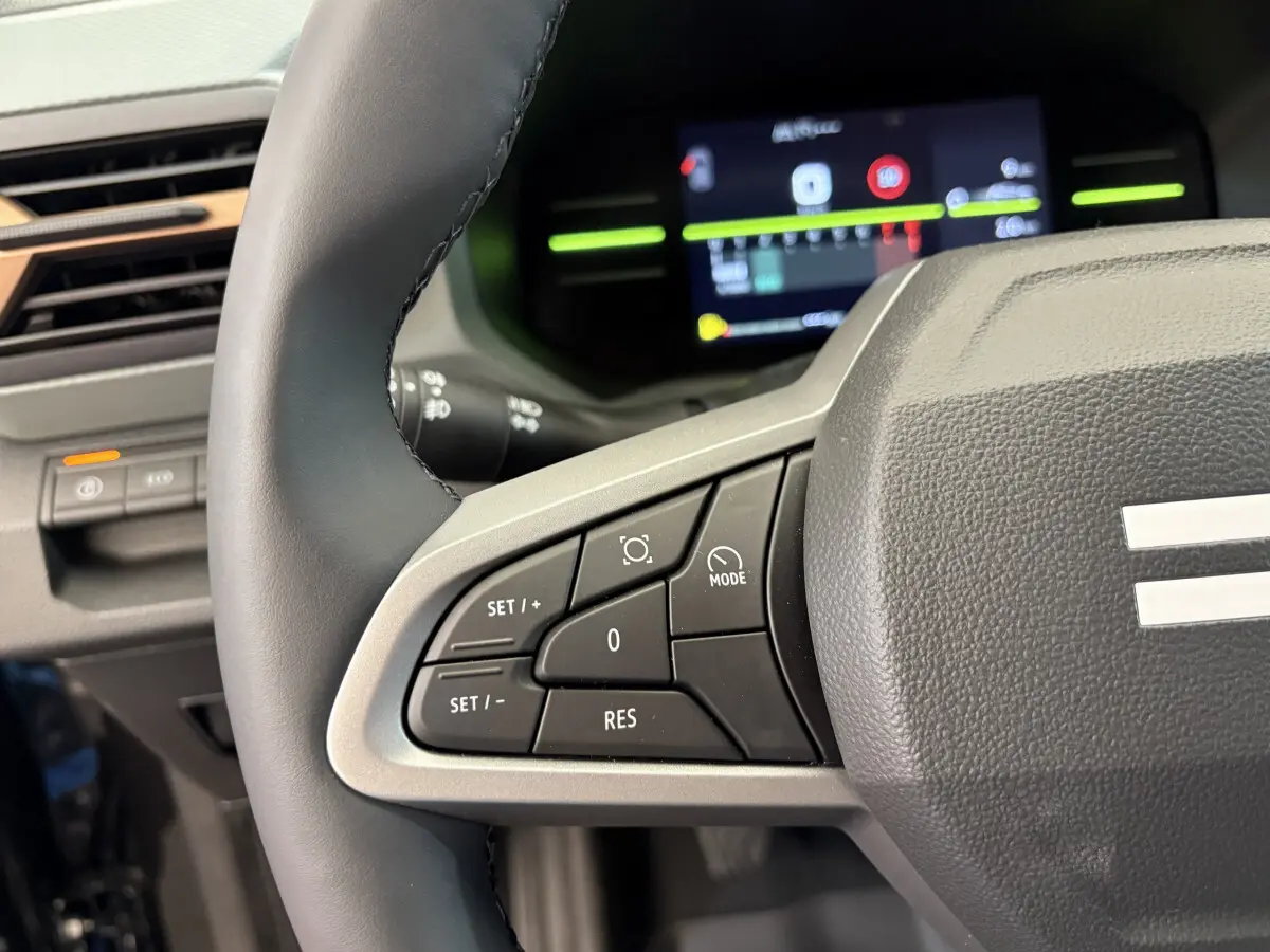 Gros plan sur le côté gauche du volant cuir du Dacia Duster 2025 avec commandes multifonctions et tableau de bord numérique.