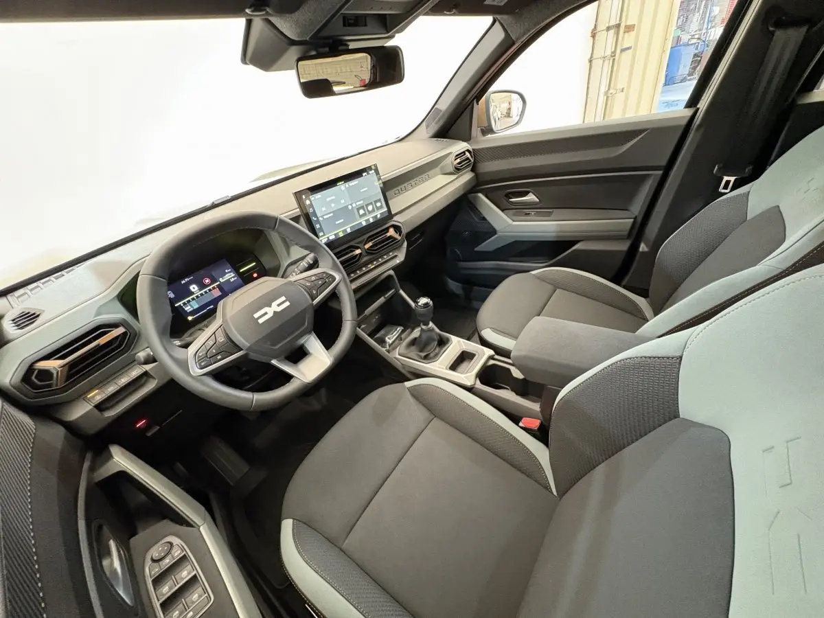 Vue intérieure avant droite du Dacia Duster 2025, tableau de bord moderne avec écran tactile et volant multifonctions noir.