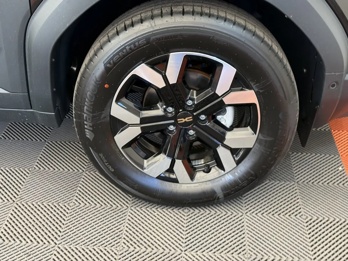 Gros plan sur la roue avant droite du Dacia Duster noir 2025 avec jante alliage bicolore et pneu Hankook.