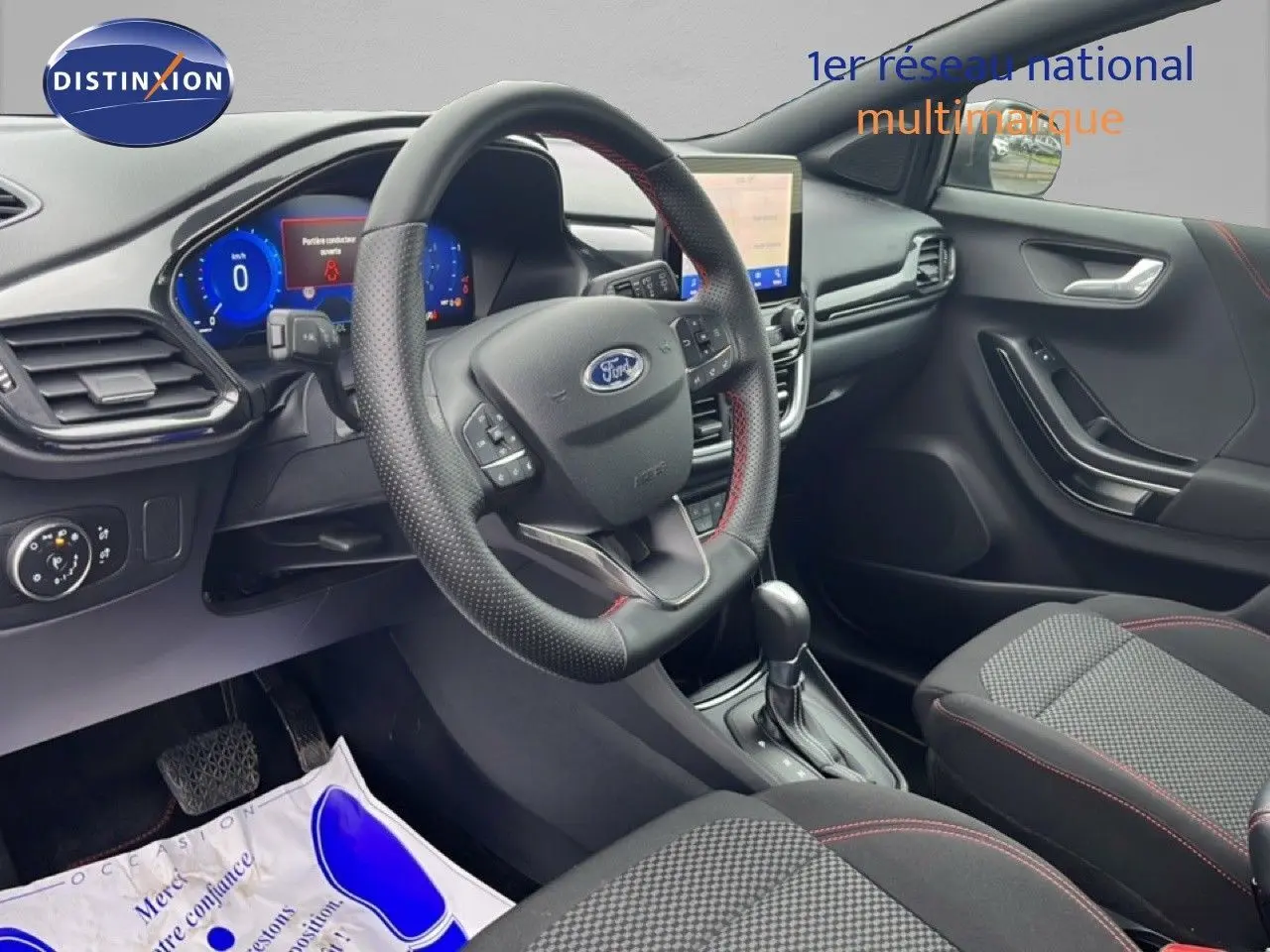 Intérieur du Ford Puma 2024 en vue côté conducteur, volant cuir noir avec surpiqûres rouges et tableau de bord digital.