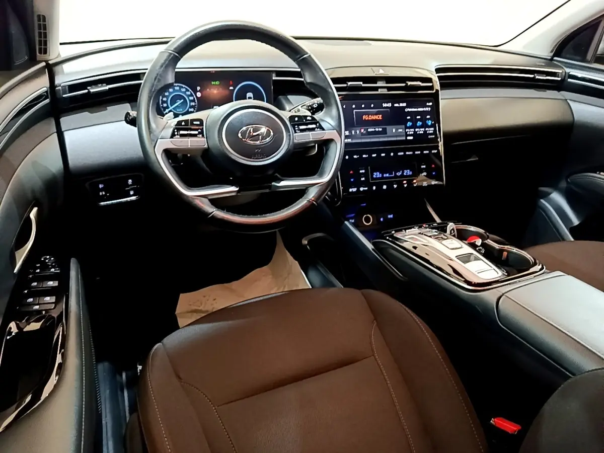 Vue intérieure avant du Hyundai Tucson 2022, tableau de bord noir avec écran tactile central et volant multifonction.