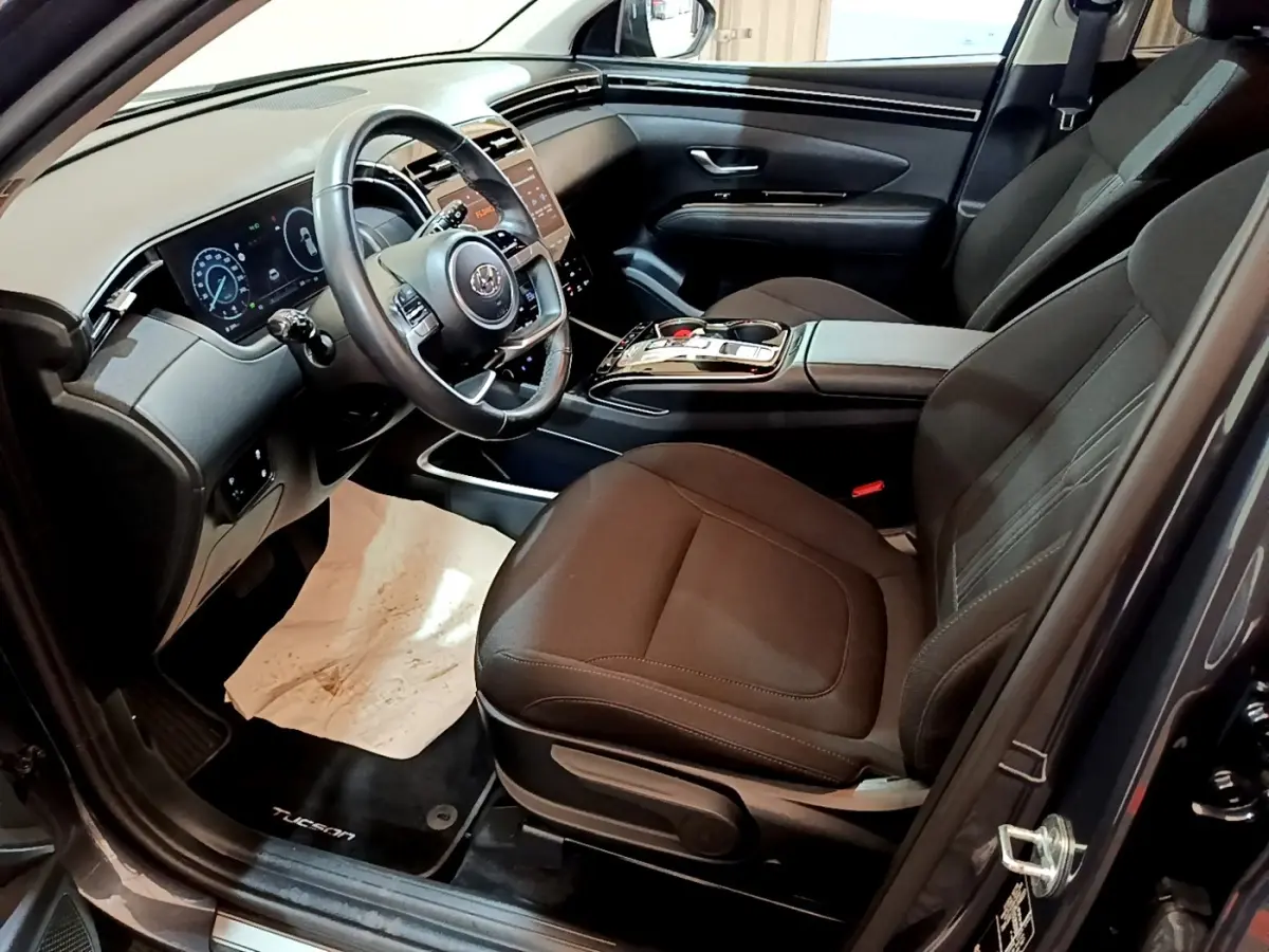 Vue intérieure côté conducteur du Hyundai Tucson 2022, sièges noirs et tableau de bord digital avec écran tactile.