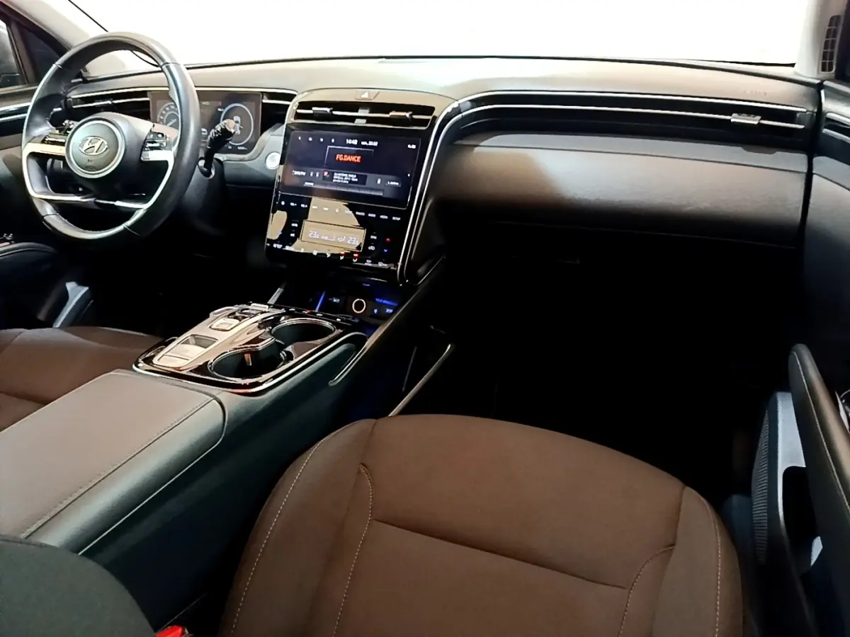 Vue intérieure côté conducteur du Hyundai Tucson 2022, tableau de bord noir avec écran tactile central et volant cuir alu.