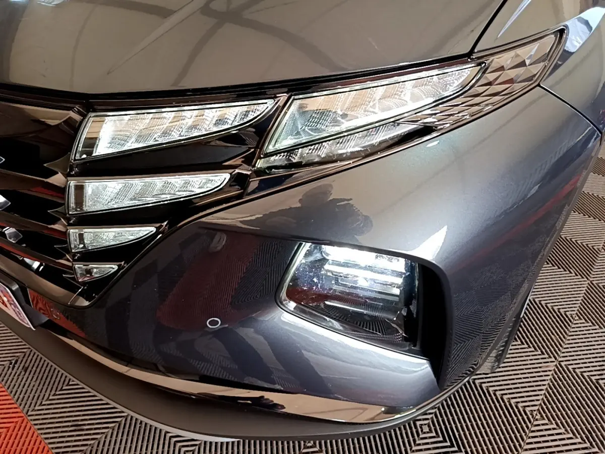 Gros plan sur l'avant droit gris foncé du Hyundai Tucson 2022, mettant en valeur les phares LED et la calandre noire brillante.
