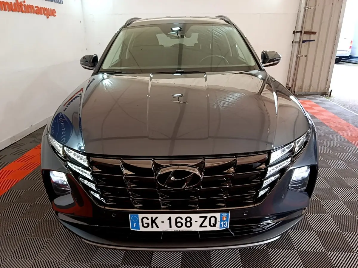 Vue avant d'un Hyundai Tucson gris foncé 2022 avec calandre noire et phares LED allumés en intérieur.
