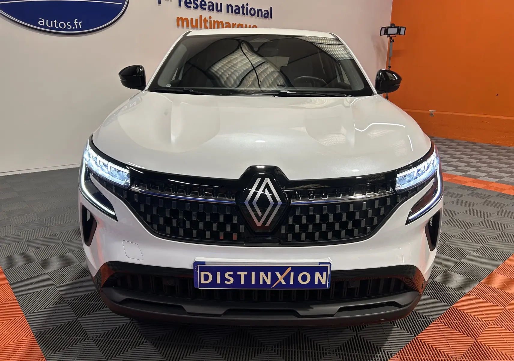 Vue avant d'un Renault Austral blanc nacré avec calandre noire et phares LED allumés en intérieur showroom.